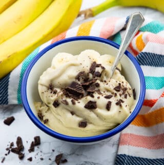 a blue and white bowl with frozen banana ice cream sprinkled with chopped dark chocolate