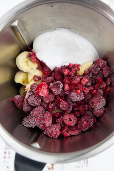 frozen raspberries, frozen bananas, and coconut yogurt in a blender on a marble countertop