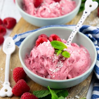 two bowls with raspberry ice cream on a wooden board with fresh raspberries on the side