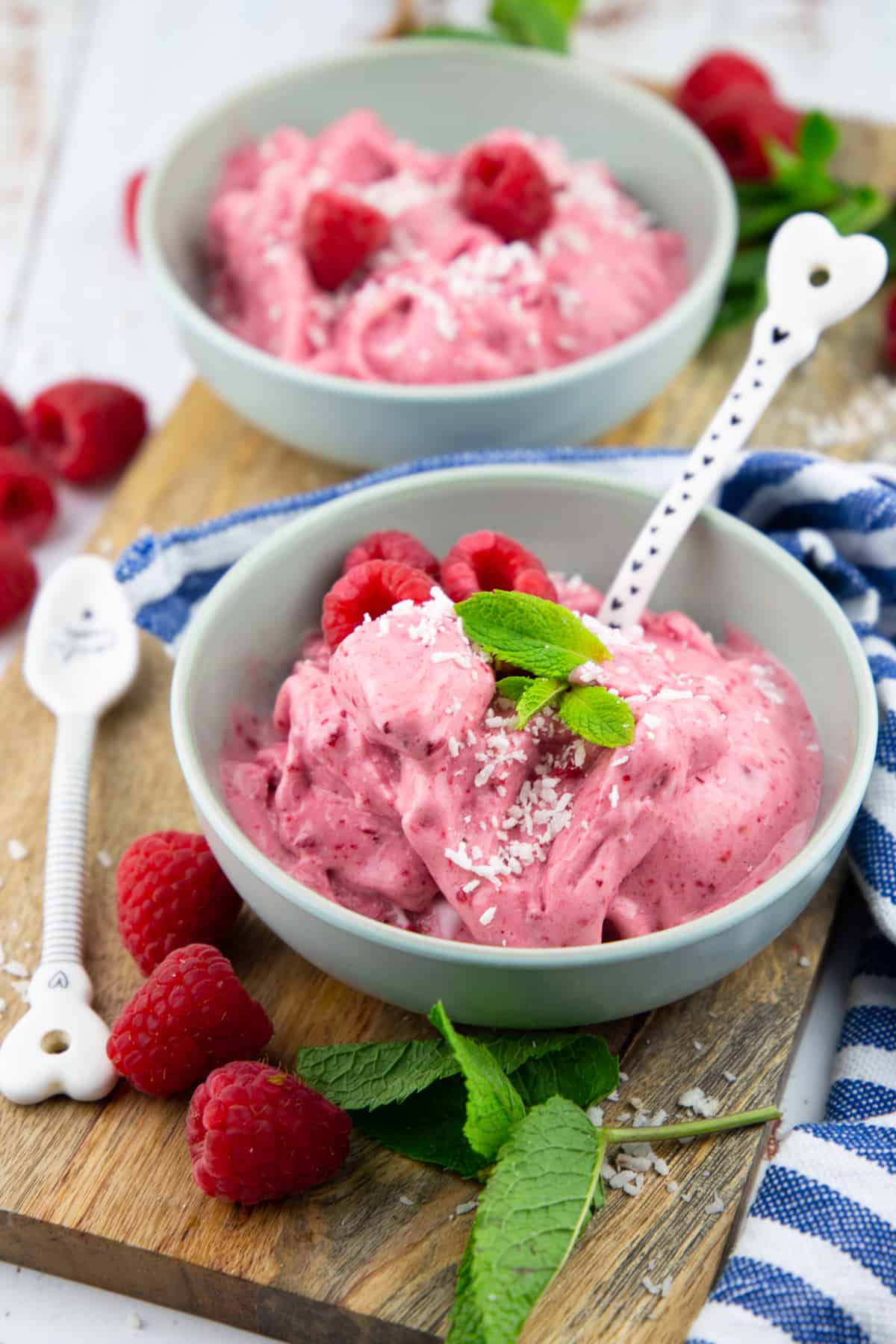 two bowls with raspberry ice cream on a wooden board with fresh raspberries on the side 