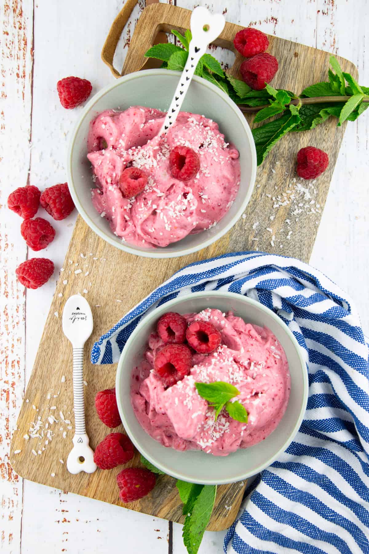 two bowls of raspberry ice cream on a wooden board with fresh raspberries and mint on the side 