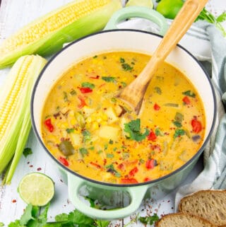 a mint green pot with summer corn chowder with a wooden spoon on a white board