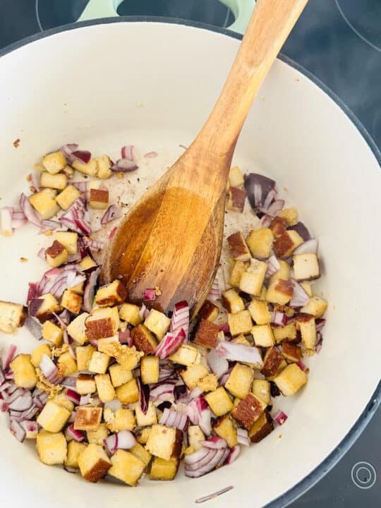 smoked tofu cubes and red onion in a white pot with a wooden spoon