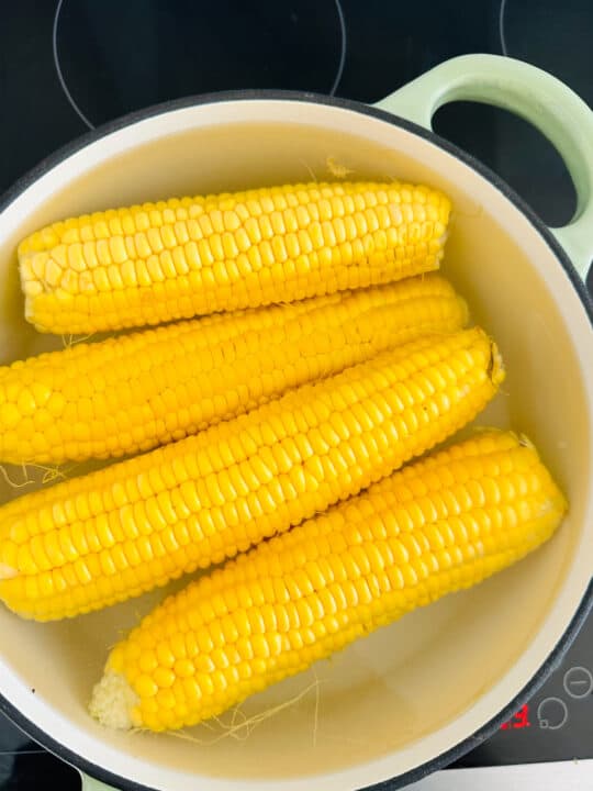 four corn cobs in a white pot on a stovetop
