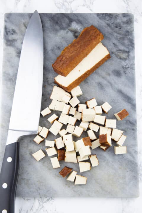 smoked tofu cubes on a chopping board with a large knife on the side