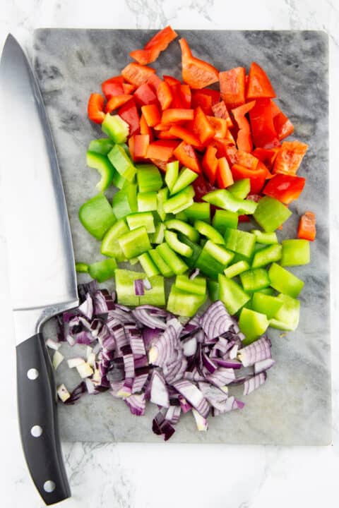 chopped bell pepper and red onion on a chopping board with a knife on the side