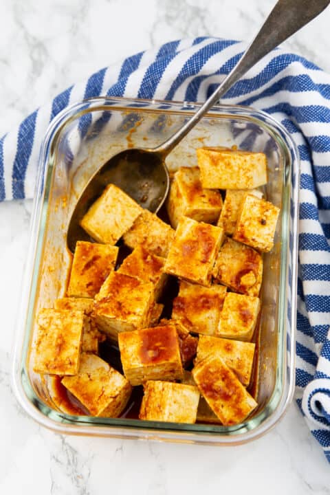 a glass container with marinated tofu cubes and a spoon