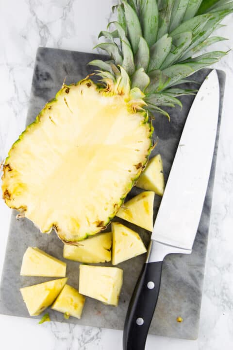 half a pineapple on a chopping board with a large knife on the side