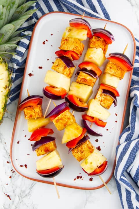 five vegetable skewers on a white plate on a marble countertop