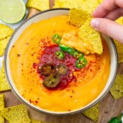 a hand dipping tortilla chips in a bowl with vegan nacho cheese