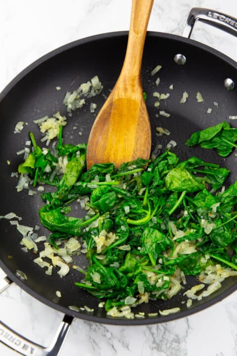 sautéd onion and spinach in a black pan on a marble countertop