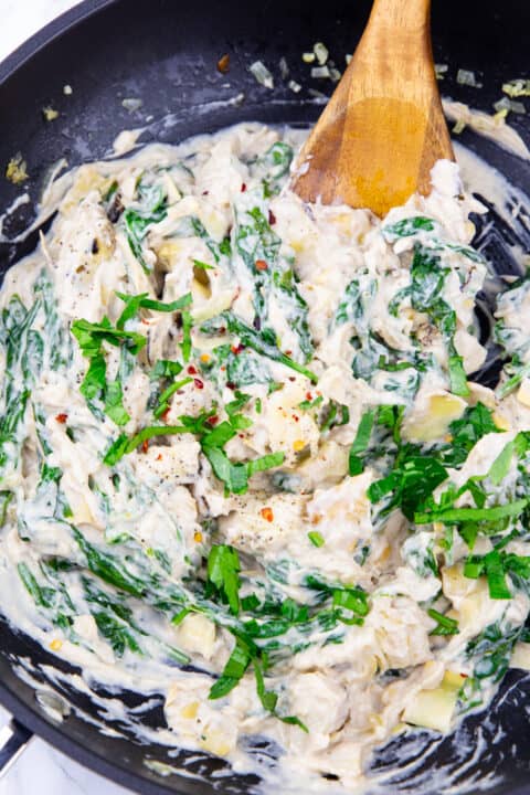 spinach artichoke dip in a black pan with a wooden spoon
