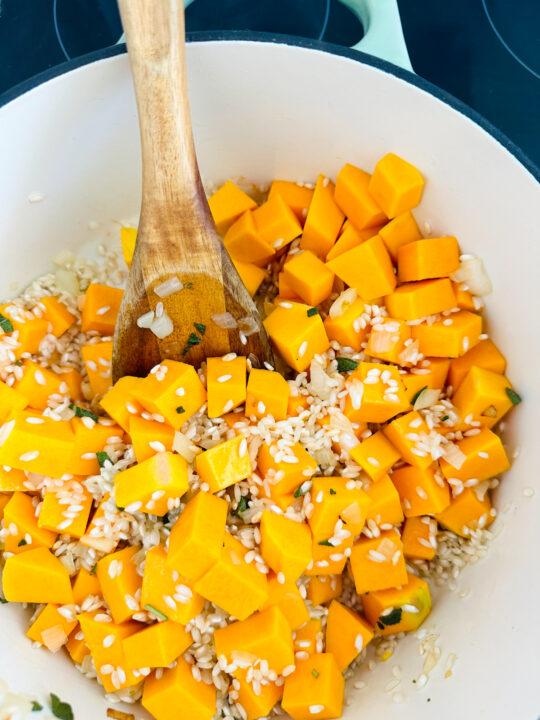cubed butternut squash with Arborio rice in a white pot with a wooden spoon