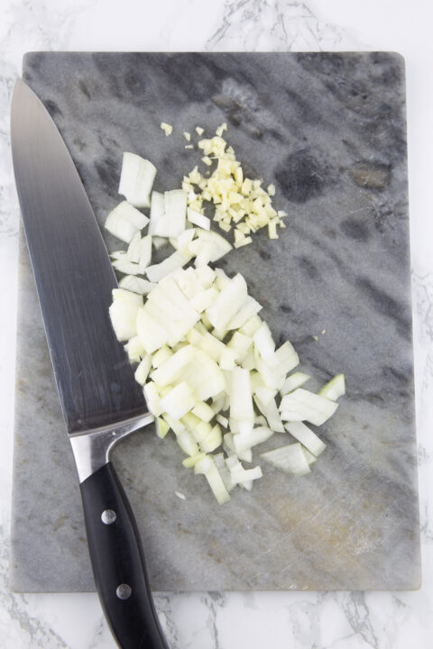 finely chopped garlic and onion on a marble chopping board with a large kitchen knife