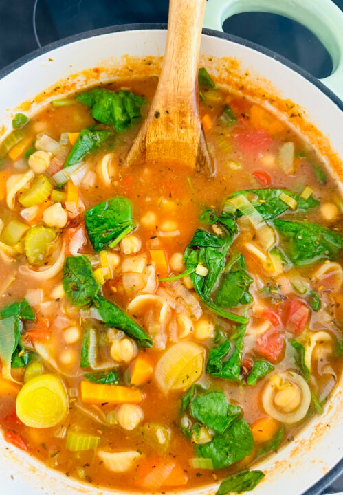 a white pot with chickpea soup with pasta, vegetables, and spinach