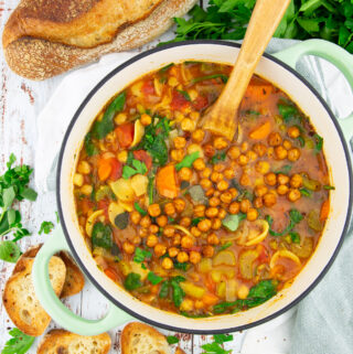 chickpea soup with carrots in a green pot on a wooden board with bread in the background