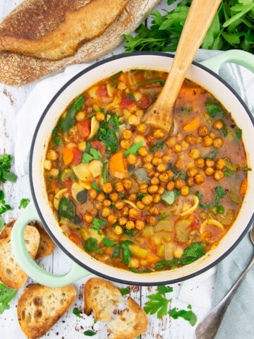 chickpea soup with carrots in a green pot on a wooden board with bread in the background