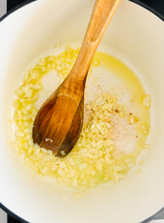 sautéd onion and garlic in a white pot with a wooden spoon