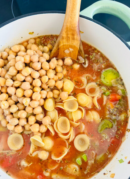 a white pot with vegetables, pasta, and chickpeas