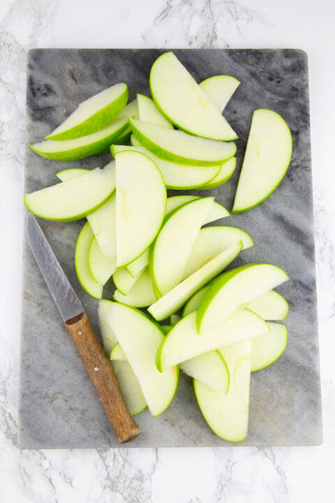 sliced apples on a marble chopping board with a knife on the side