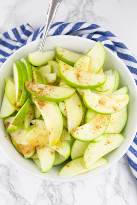 sliced apples in a white bowl sprinkled with cinnamon