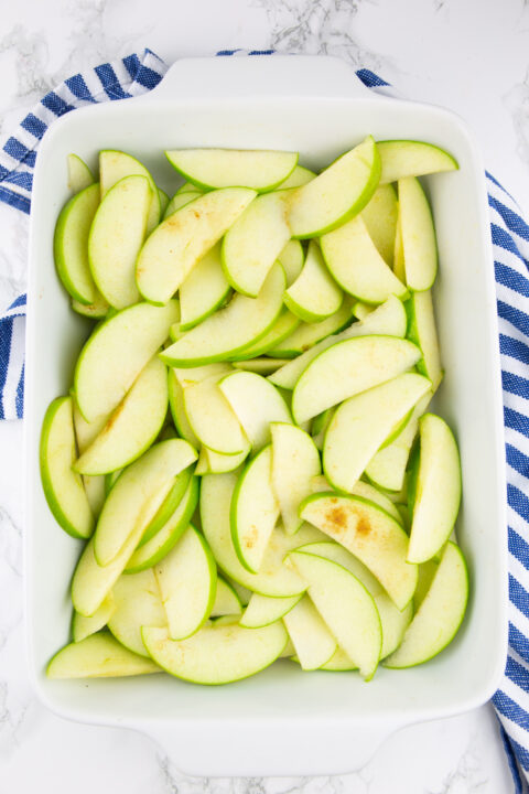 sliced Granny Smith apples in a white baking dish on a marble countertop