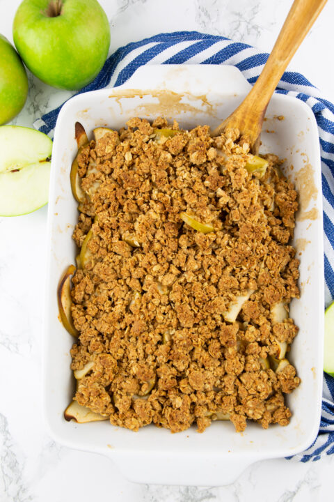 vegan apple crips in a white baking dish on a marble countertop after baking