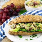 a white plate with a bun with vegan chicken salad with grapes and another bun in the background