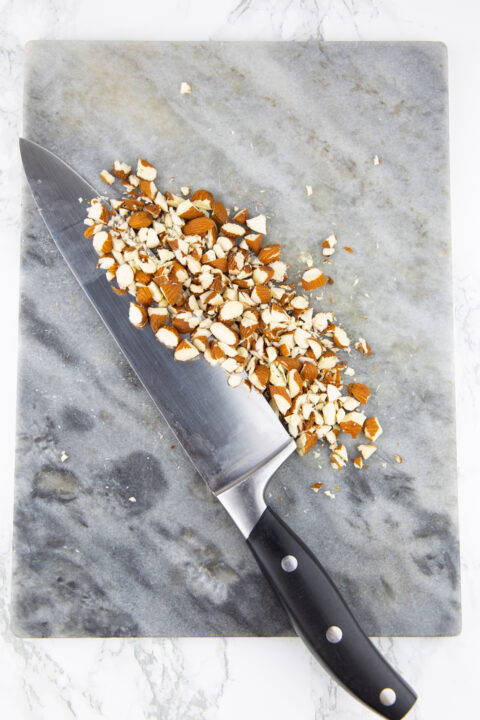 roughly chopped almonds on a cutting board with a knife