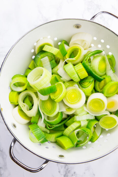 sliced leek in a white colander on a marble countertop