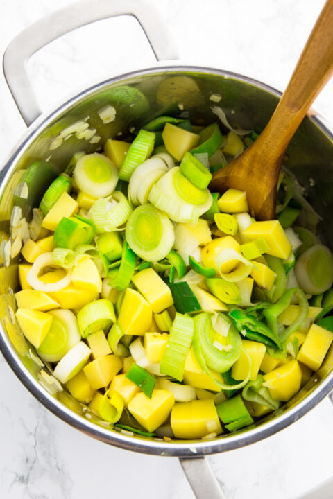 cubed potatoes and leek in a pot with a wooden spoon 