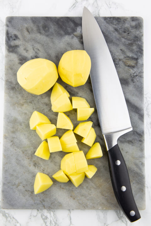 cubed potatoes on a marble chopping board with a large knife on the side