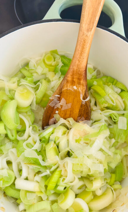 cooked leek in a white pot with a wooden spoon