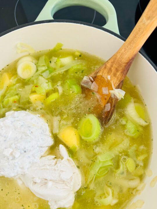 a green and white pot with potatoes and leek in vegetable broth