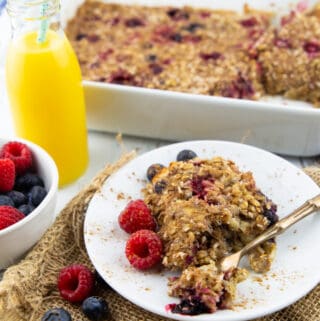 vegan baked oatmeal on a white plate with berries on the side and a white casserole dish in the background