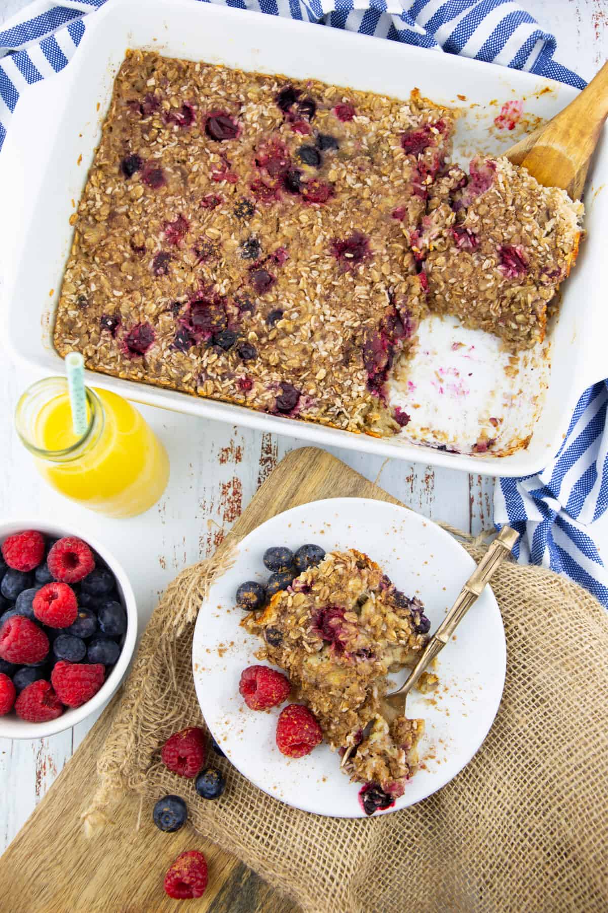 a white casserole dish with baked oatmeal with a small plate and a bowl with berries on the side