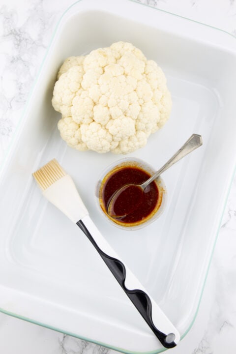 a whole cauliflower in a white steel sheet pan on a marble countertop 