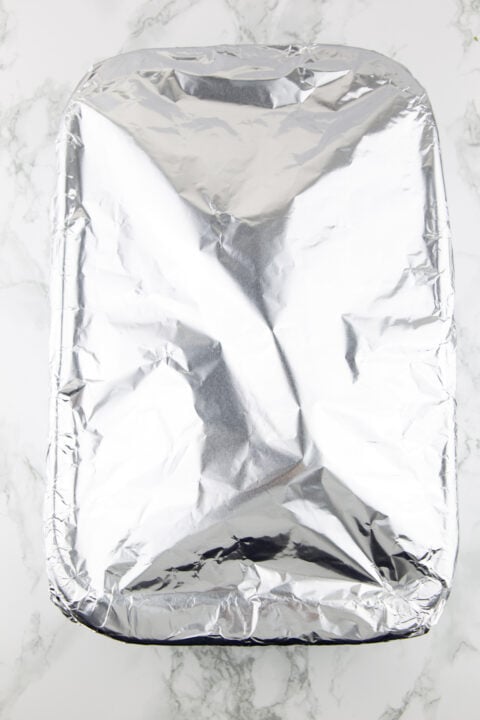 a baking pan covered with aluminium foil on a marble countertop 
