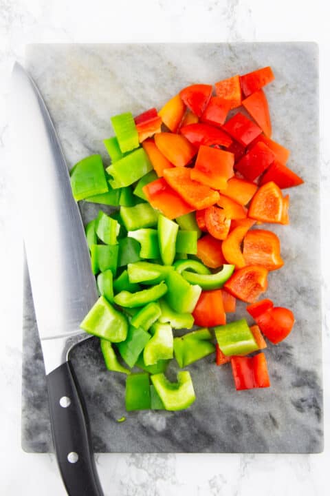 diced red and green bell pepper on a marble chopping board with a large knife 