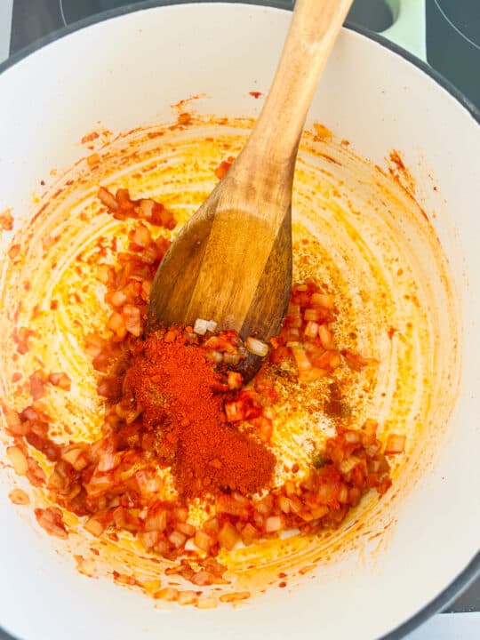 sautéd onion with tomato paste and spices in a white pot with a wooden spoon 