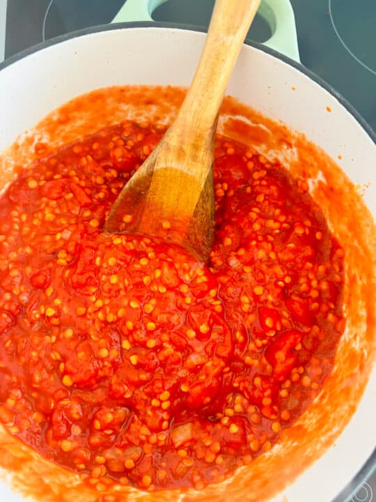 red lentils with diced tomatoes and vegetable broth in a white pot with a wooden spoon
