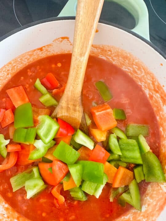 a white pot with red lentils with diced tomatoes and red and green bell pepper with a wooden spoon 