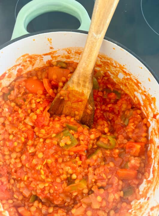 a white pot with cooked lentils with bell peppers in tomato sauce 