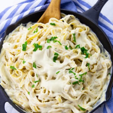 vegan Alfredo sauce with fettuccine in a black cast iron pan on a marble countertop