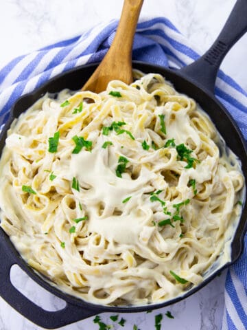 vegan Alfredo sauce with fettuccine in a black cast iron pan on a marble countertop