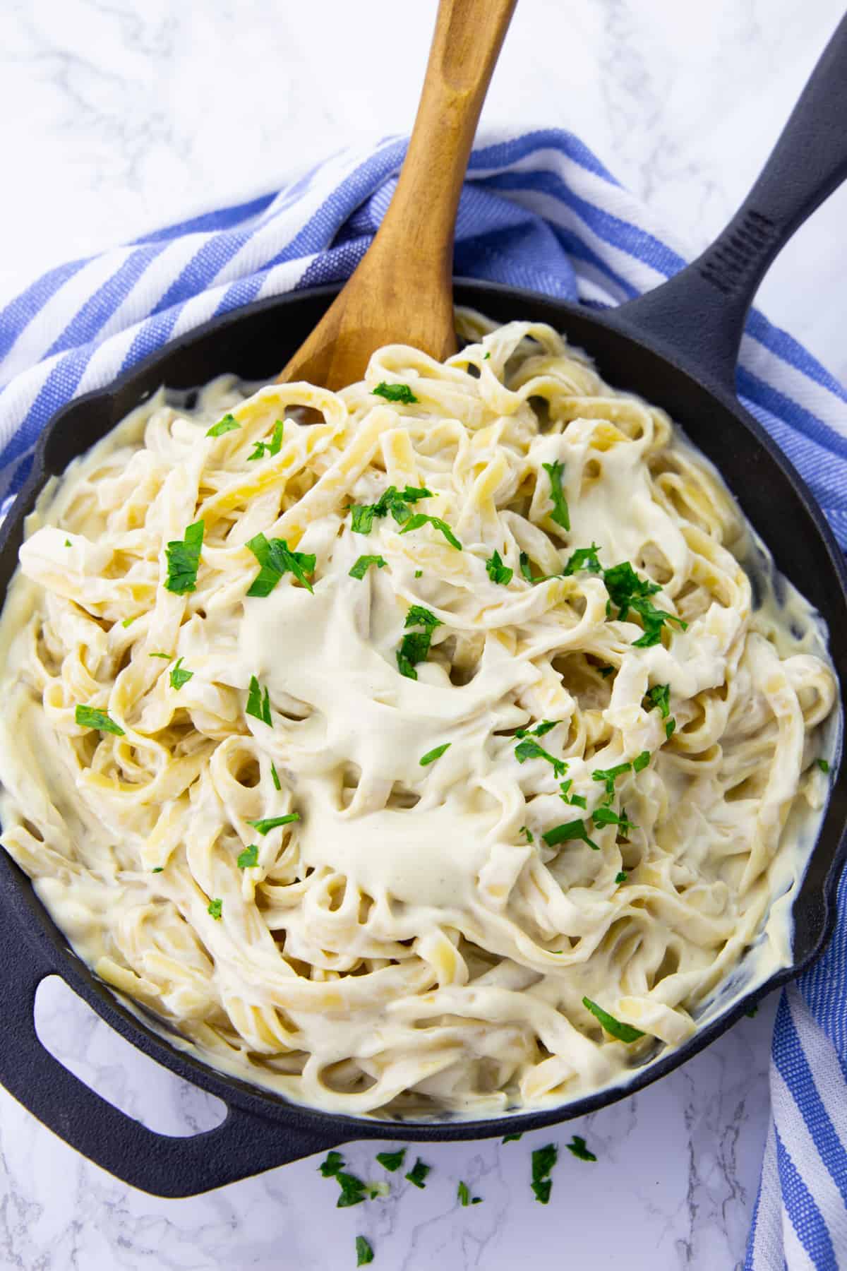 vegan Alfredo sauce with fettuccine in a black cast iron pan on a marble countertop 