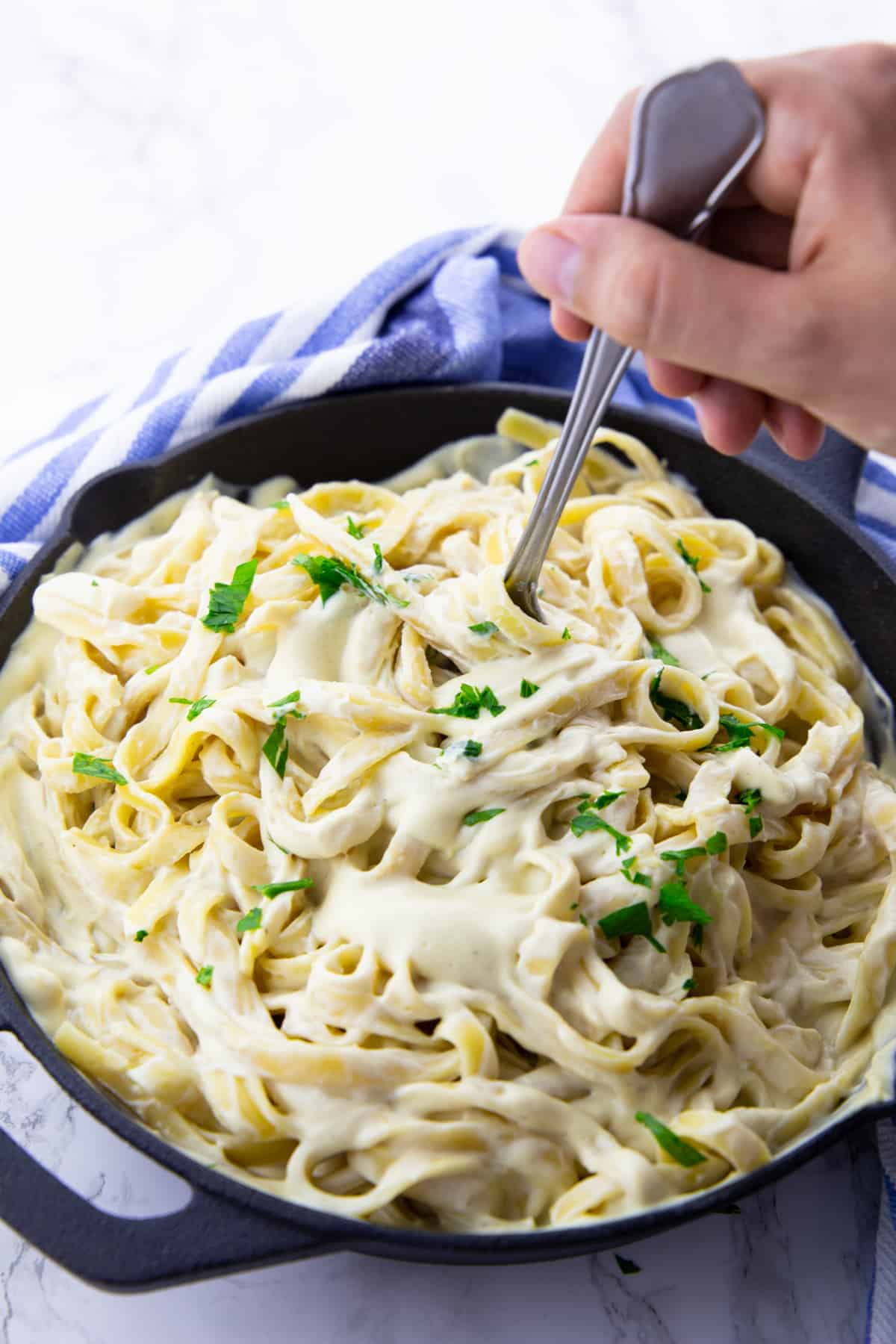 a hand rolling up fettuccine in a creamy sauce with a fork 
