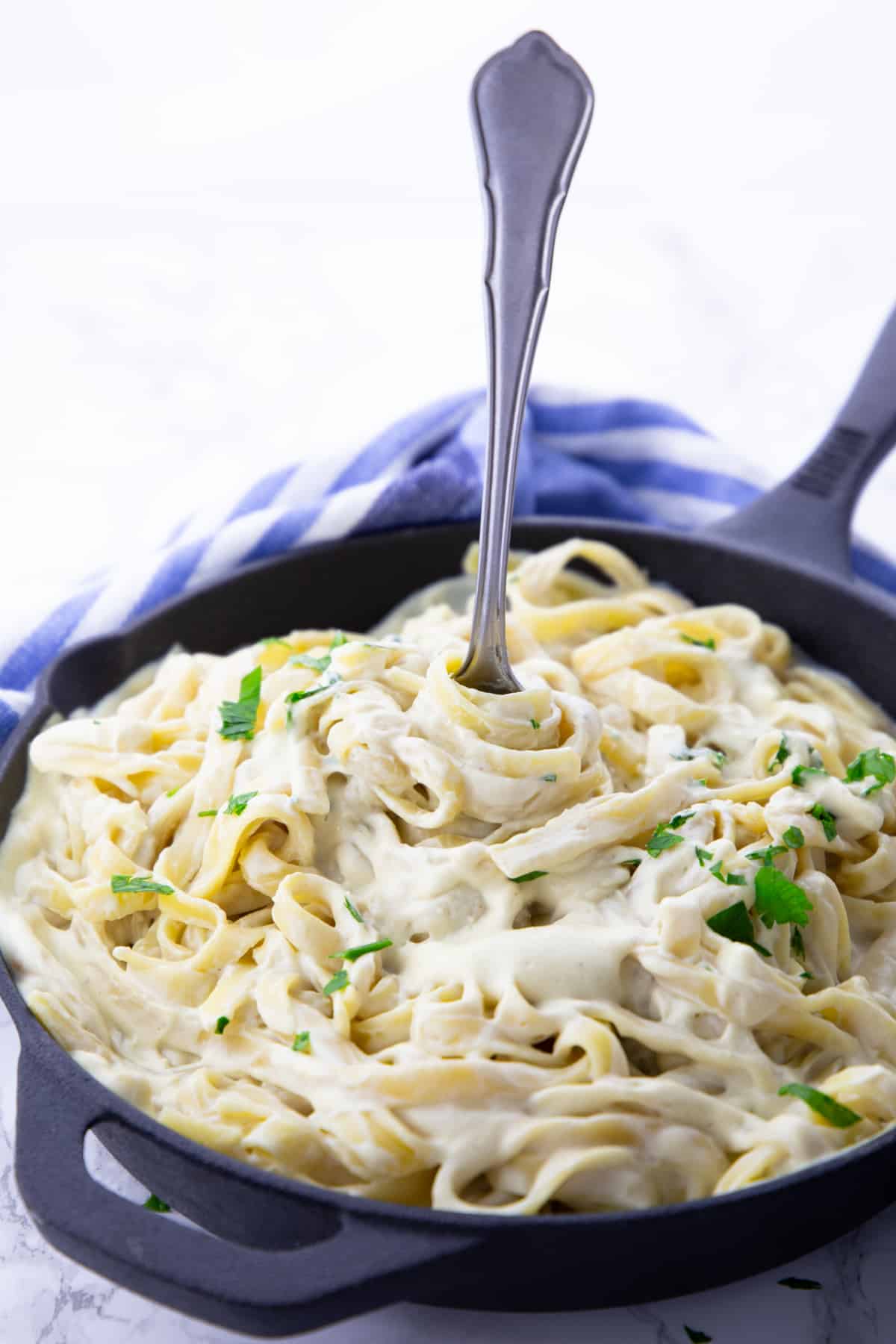 creamy fettuccine Alfredo in a black cast iron pan with a fork 