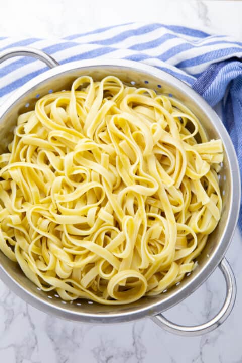 cooked fettuccine in a colander on a marble countertop