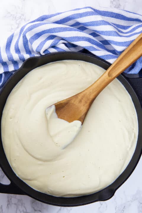 creamy vegan Alfredo sauce in a black cast iron pan with a wooden spoon